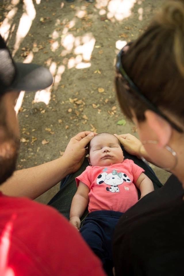 Mom and dad holding baby in pink shirt with their hands placed on babies head