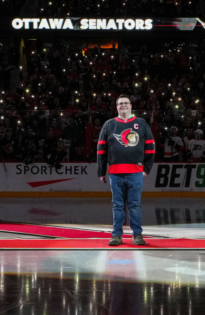 Man in a Ottawa Senators jersey standing on a red carpet placed on skating ice